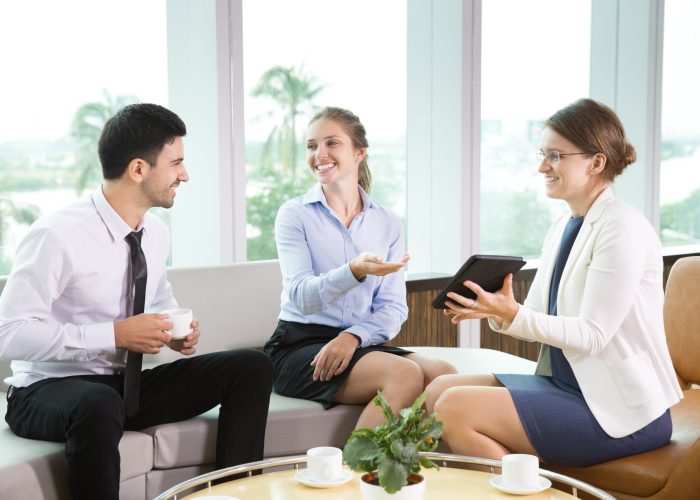 Business People Sitting in Modern Office Group of three young business people sitting in modern office and having informal meeting. Businesswoman showing something on tablet computer to her colleagues, they smiling